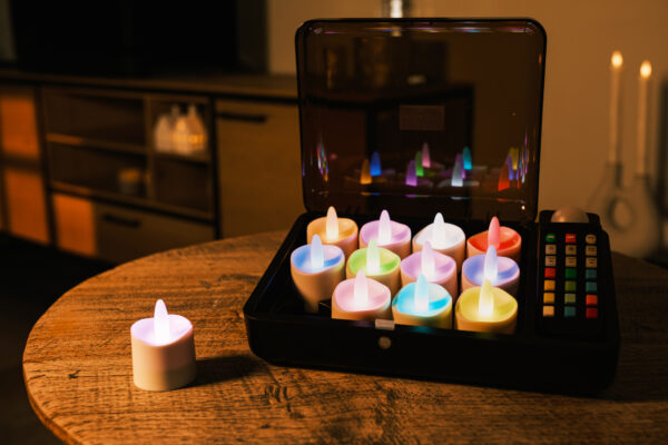 RGB LED-värmeljus DORSETTO (12 st) i öppen svart laddbox på runt träbord – med fjärrkontroll