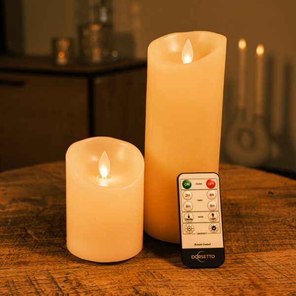 Två uppladdningsbara LED-vaxljus från DORSETTO i olika höjder på träbord med fjärrkontroll och mjuk bakgrundsbelysning