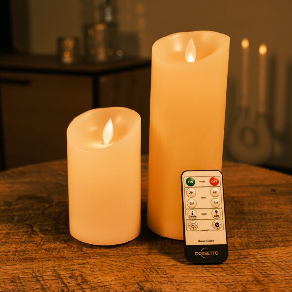 Två uppladdningsbara LED-vaxljus från DORSETTO i olika höjder på träbord med fjärrkontroll och varm belysning