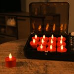 Een oplaadkoffer met 12 LED-kaarsjes rood oplaadbaar (waterdicht, timerfunctie, 175 uur, met afstandsbediening) staat open op een houten tafel, één kaars gloeit buiten; de schemerige kamer is versierd met meer kaarsen zonder vlam.