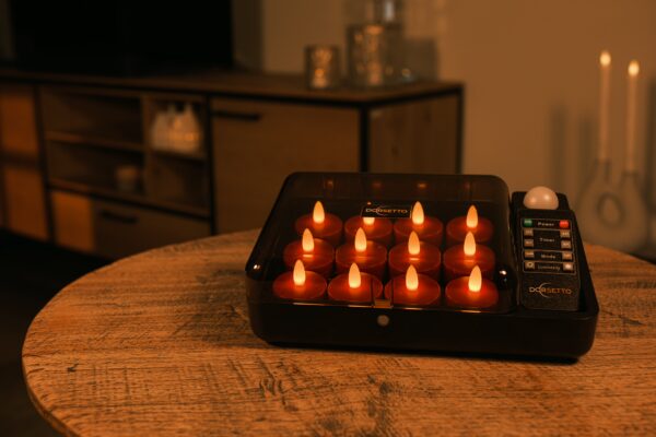 Een zwart dienblad met 12 oplaadbare rode LED-kaarsjes (175 uur, waterdicht, timerfunctie) en een afstandsbediening staat op een houten tafel in een gezellige, warm verlichte woonkamer.