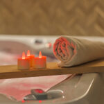 3 rode waxinelichtjes met een opgerolde handdoek op een plank bij een bad