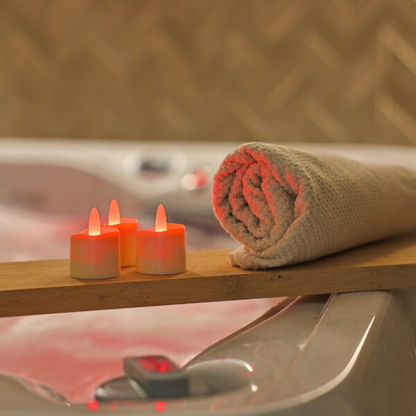 3 rode waxinelichtjes met een opgerolde handdoek op een plank bij een bad