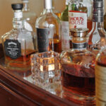 een glazen kaarsen houder met waxinelichtje er in bij flessen wiskey