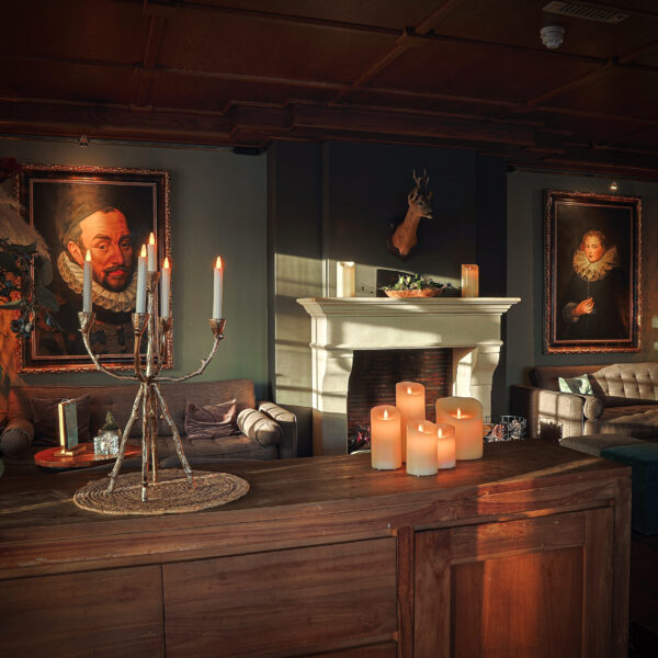 een kaarsen set en kaarsen houder op een tafel in een woonkamer met schilderijen aan de muur.