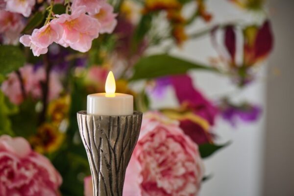 waxinelichtje met kaarsvet op houder op de achtergrond zijn roze bloemen te zien