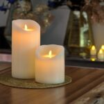 2 kaarsen van dorsetto op een onderzetter op tafel met op de achtergrond meer kaarsen en bloemen