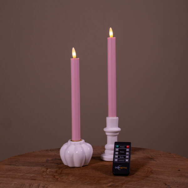 Två LED-dinerljus i mjukt rosa (set med 2, upp till 400 timmars brinntid) placerade i vita hållare på ett träunderlag, med fjärrkontroll framför. Bakgrunden är enfärgat brun.