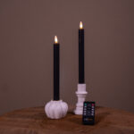 Två uppladdningsbara LED-dinerljus (set om 2, 400 timmars brinntid) placerade i vita ljushållare – en pumpaformad och en cylindrisk – på en träyta, med fjärrkontroll framför och enfärgad bakgrund.