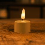 Ett litet batteridrivet LED-ljus med varm glödande låga placerat på en träyta och skapar en mysig och mjuk belysning.Ett litet batteridrivet LED-ljus med varm glödande låga placerat på en träyta och skapar en mysig och mjuk belysning.