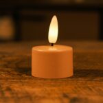 Ett litet LED-ljus med varm gul låga placerat på en träyta och skapar en mysig och stämningsfull atmosfär.