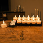 Tolv uppladdningsbara värmeljus med realistiska 3D-flammor, 140 timmars brinntid och fjärrkontroll står på ett träbord och ger ett mjukt, mysigt sken i bakgrunden.