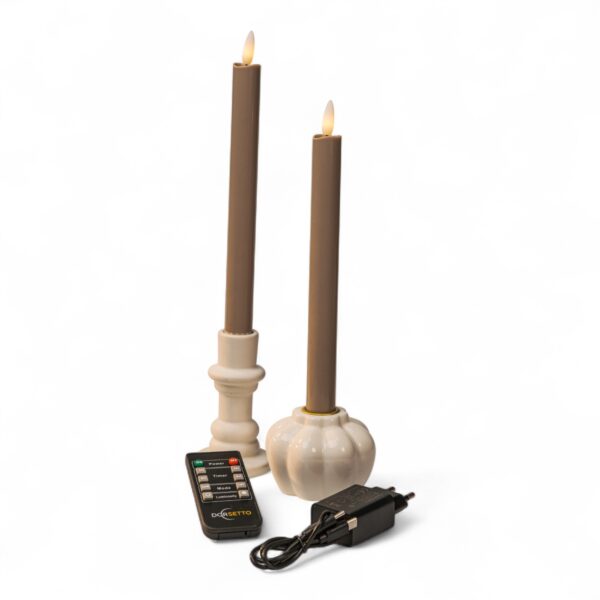 Två beige flamlösa koniska LED-ljus i vita ljushållare visas tillsammans med en svart fjärrkontroll och en svart nätadapter mot en vit bakgrund.