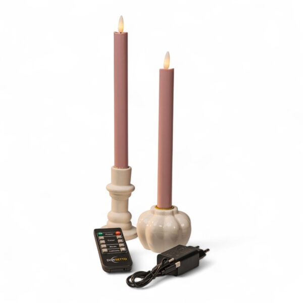 Två mjukt rosa LED-dinerljus i vita hållare tillsammans med fjärrkontroll och svart nätadapter mot vit bakgrund. Ljusen har realistiska flamformade toppar.