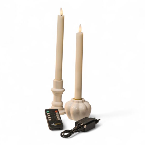 Två krämvita LED-dinerljus med realistisk låga i vita hållare, tillsammans med svart fjärrkontroll och nätadapter mot vit bakgrund.