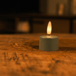 Ett set med 12 olivgröna LED-värmeljus med fjärrkontroll står på en träyta, sprider ett varmt och mjukt sken i upp till 400 timmar och skapar en mysig, intim atmosfär med sitt behagliga ljus.