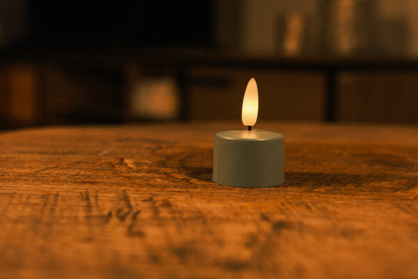 Ett set med 12 olivgröna LED-värmeljus med fjärrkontroll står på en träyta, sprider ett varmt och mjukt sken i upp till 400 timmar och skapar en mysig, intim atmosfär med sitt behagliga ljus.