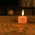 Ett set med 12 rosa uppladdningsbara värmeljus med mjuk gul LED-flamma och fjärrkontroll står på ett träbord. Varje värmeljus har en brinntid på upp till 400 timmar och skapar stämningsfull belysning i hemmet.