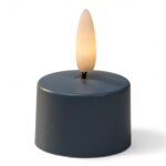 Ett litet, runt, mörkfärgat LED-värmeljus med plastlåga, tänt för att likna ett riktigt ljus, mot en vit bakgrund.