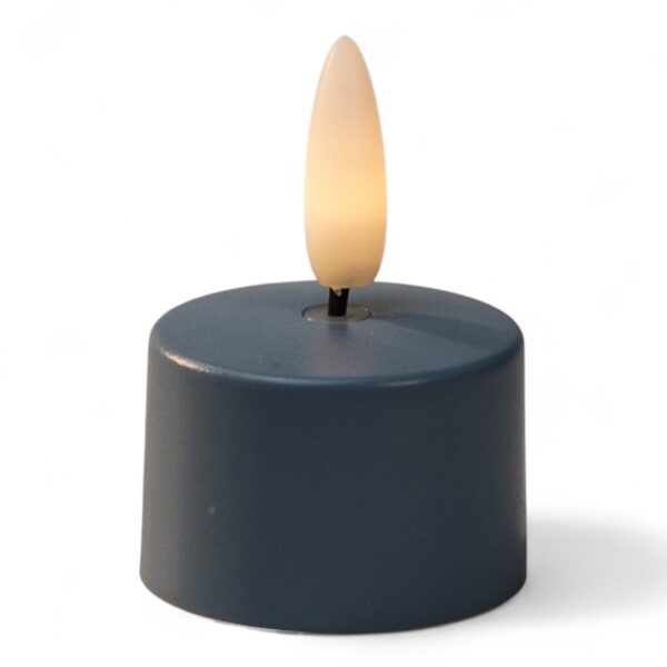 Ett litet, runt, mörkfärgat LED-värmeljus med plastlåga, tänt för att likna ett riktigt ljus, mot en vit bakgrund.