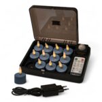 En svart laddbox med 12 blå uppladdningsbara LED-värmeljus (Stone Bleu No.86, brinntid upp till 400 timmar), en fjärrkontroll, ett värmeljus utanför boxen samt en svart nätadapter med kabel placerad framtill.